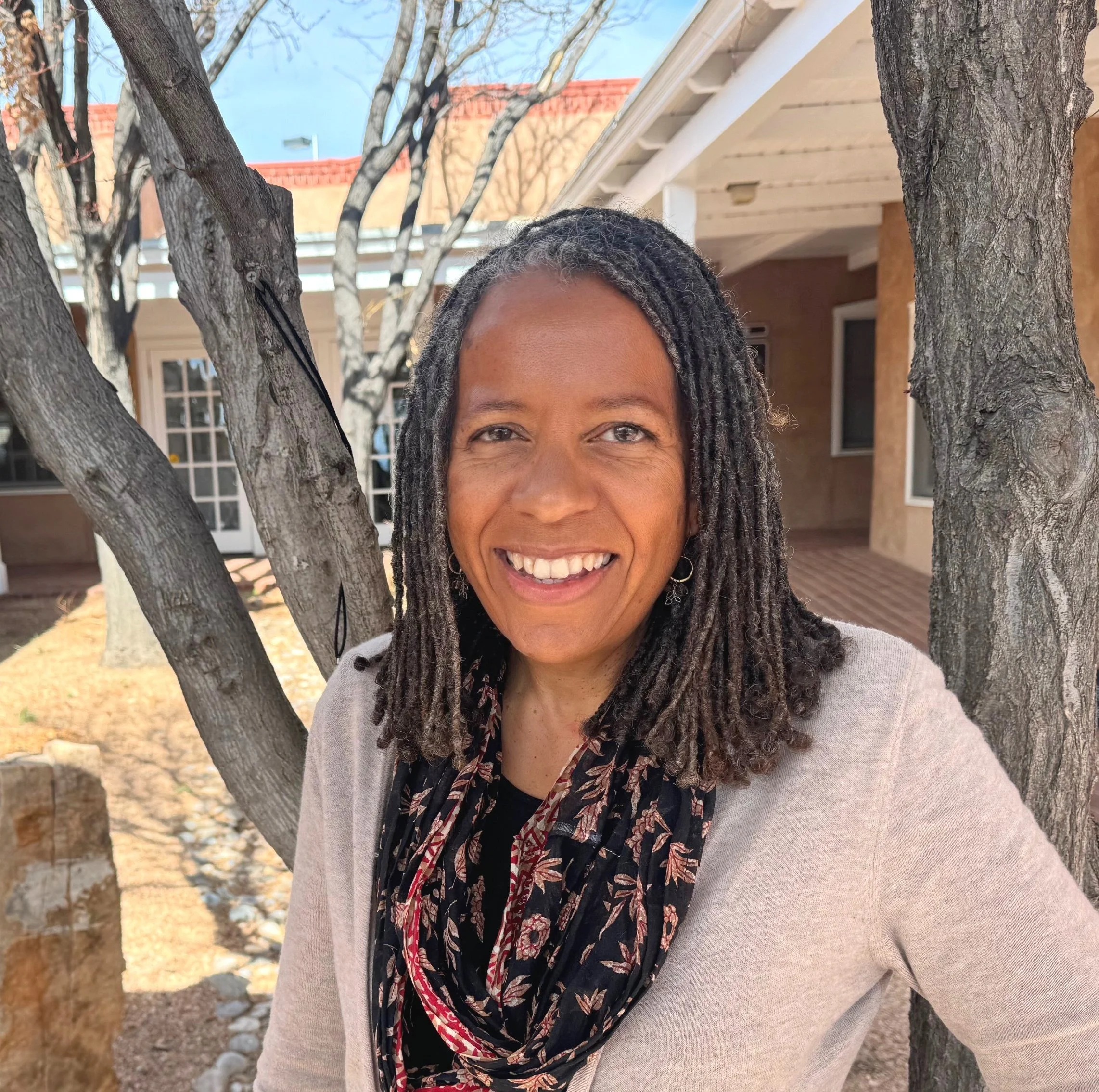 Sarah Hobongwana (also known as Lindi Hobongwana) has dark, shoulder length dreads and is wearing a floral scarf while smiling. 