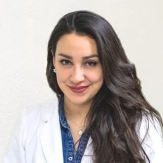 Grecia Heredia, a woman with long black hair, wears a white medical coat and smiles.