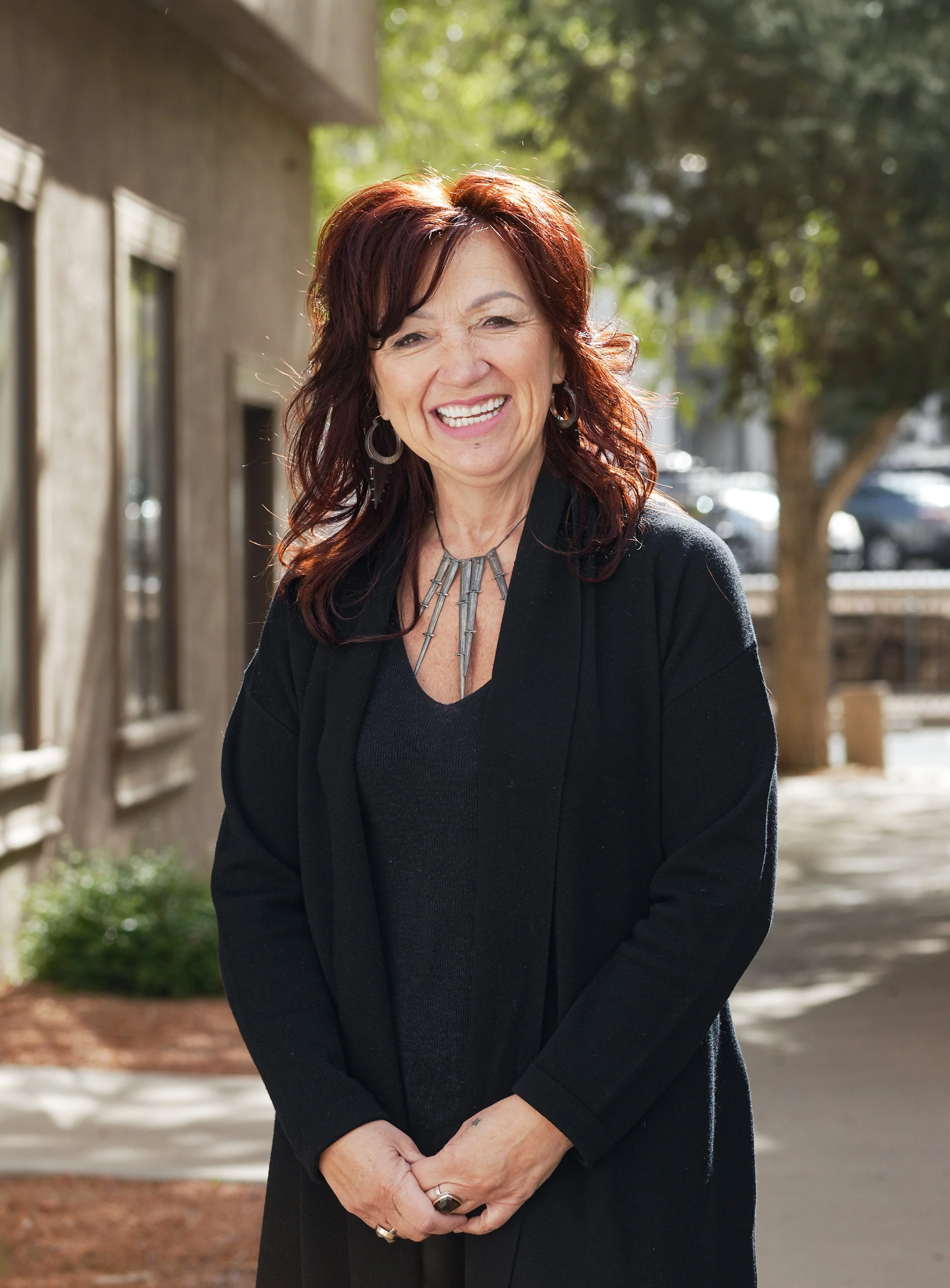 Wenoah Veikley, a woman with curled longer reddish brown hair, wears a black sweater and smiles at us.