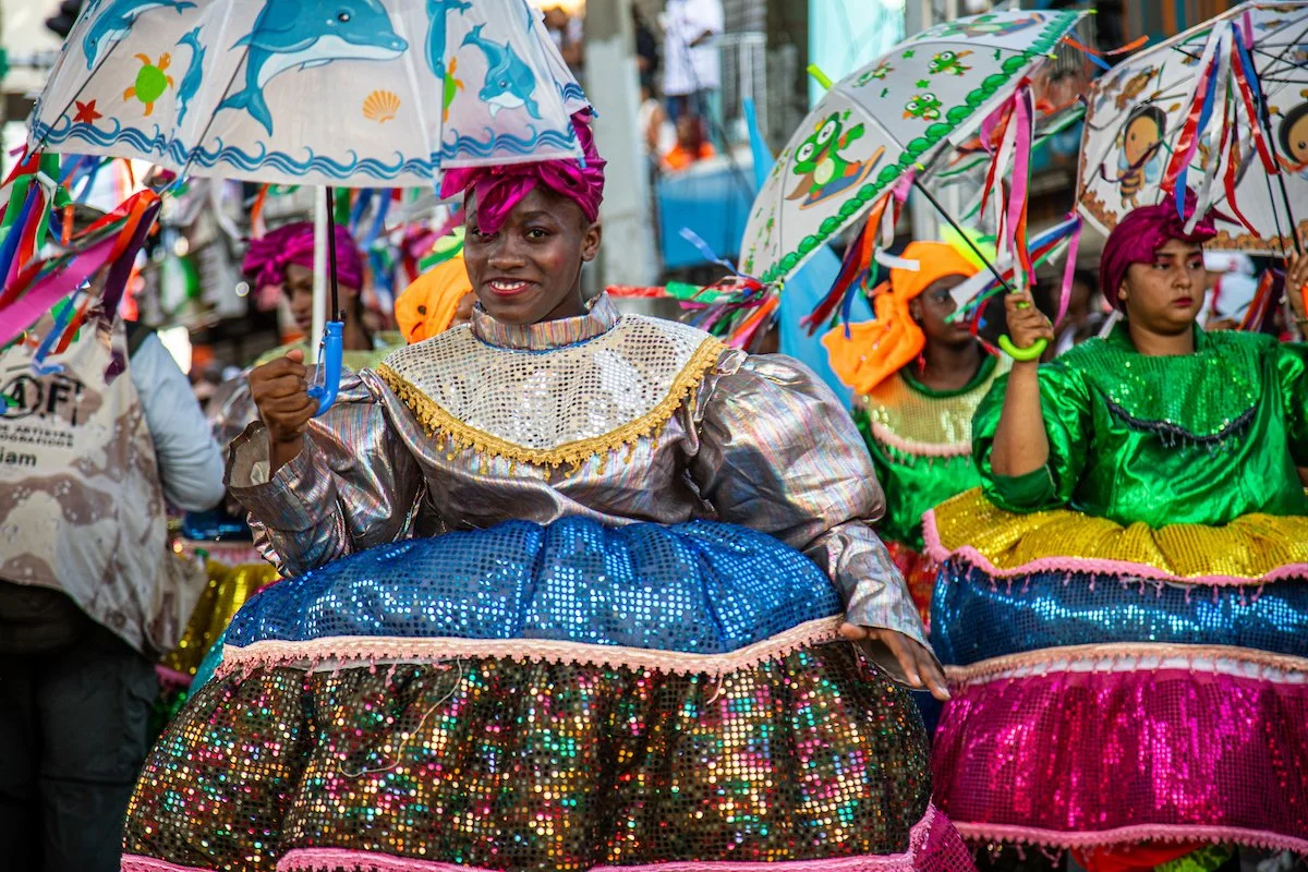 Women dressed in colorful traditional costumes holding umbrellas during a cultural parade or festival.