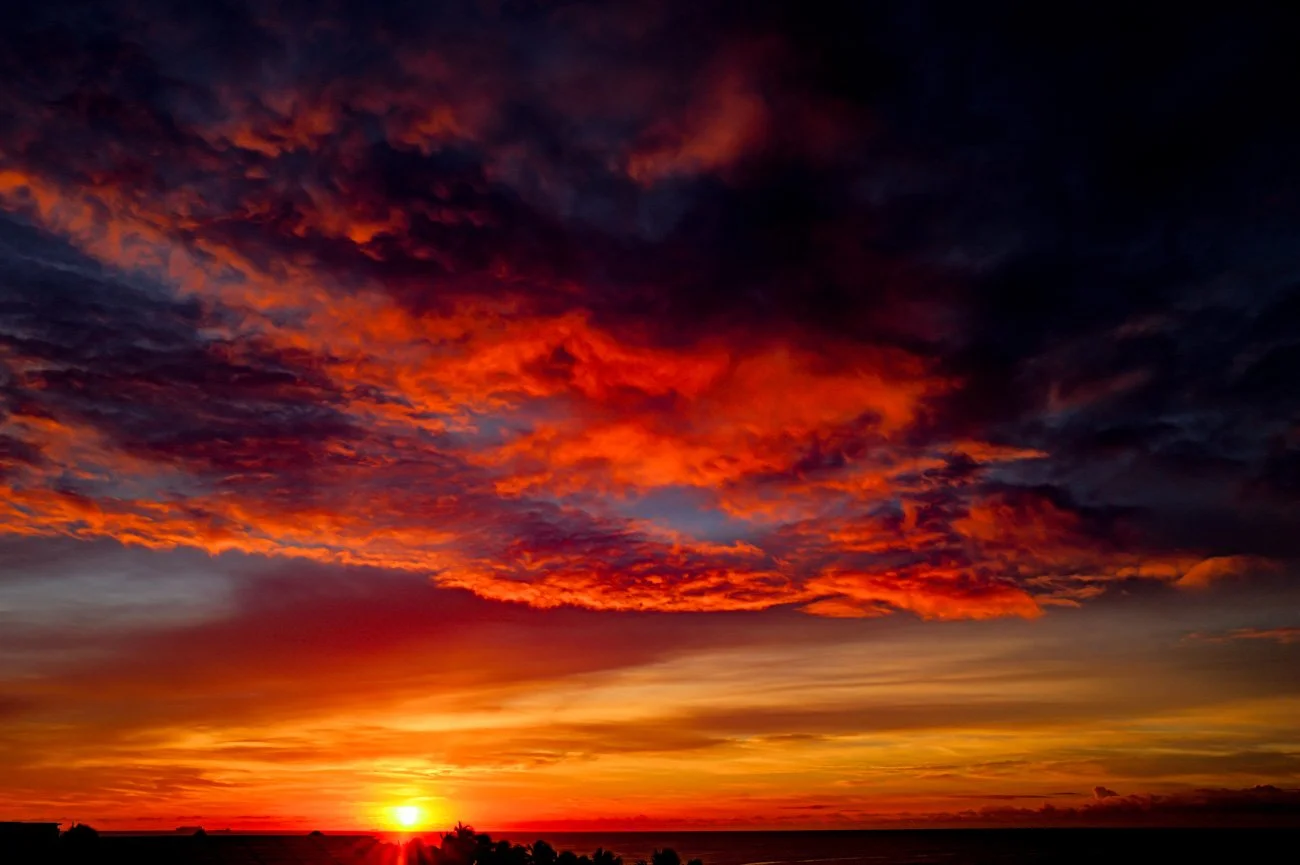 Vivid sunset over the ocean with colorful clouds in shades of orange, red, purple, and yellow.