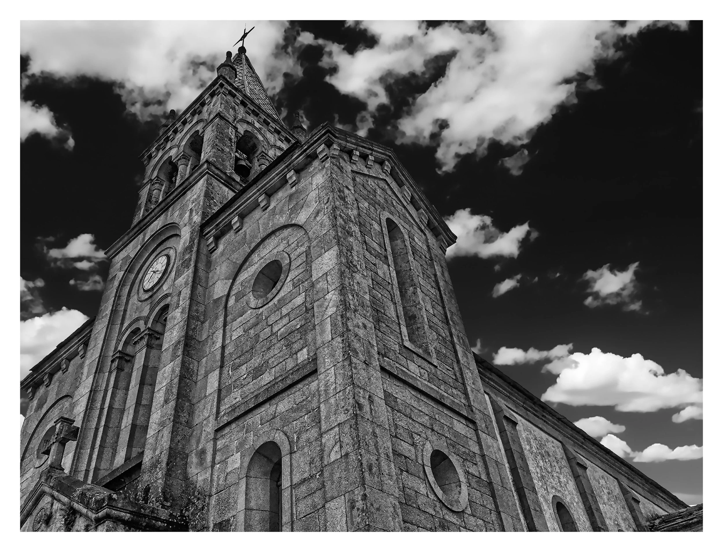 Black and white photo of a historic stone church with a tall steeple against a cloudy sky.