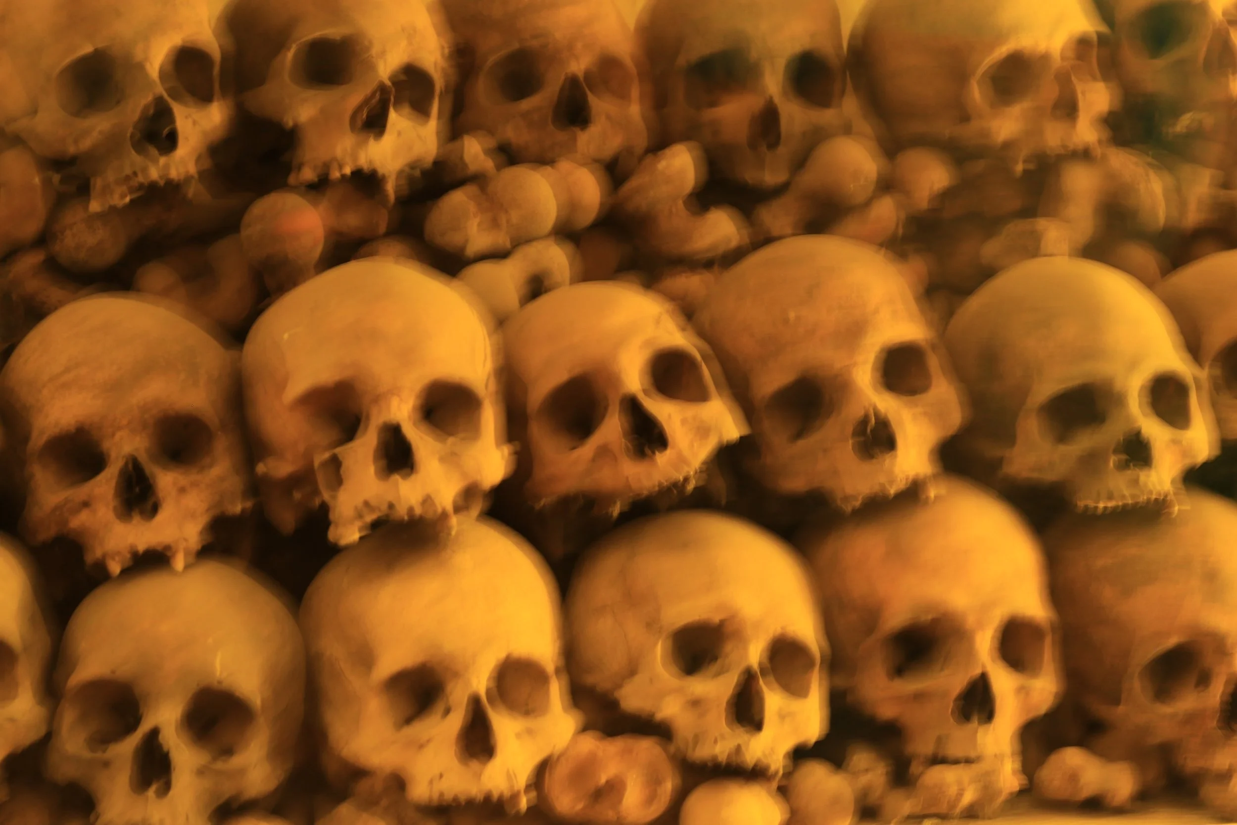 Multiple human skulls stacked in a dark, reddish-orange setting.