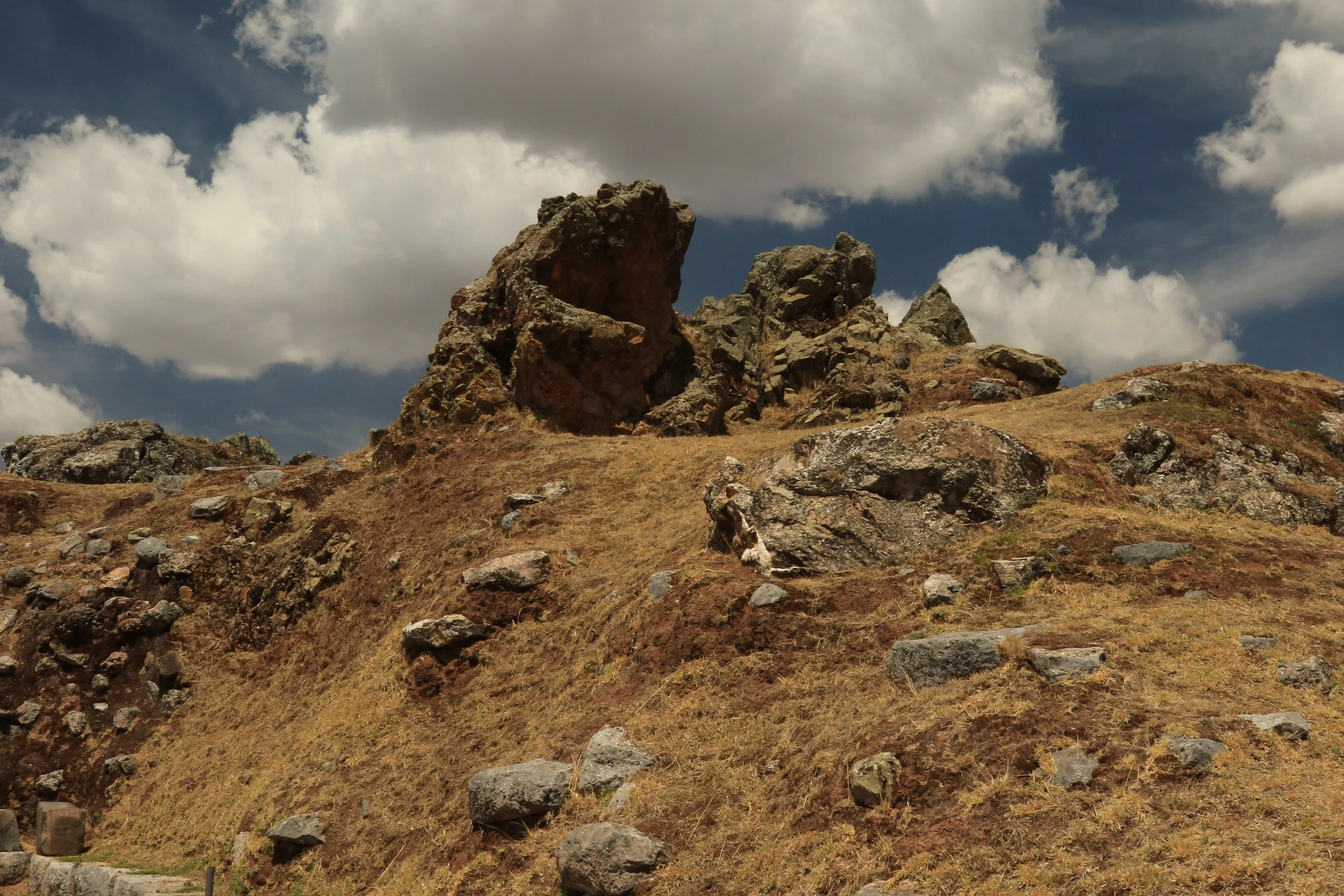 Barren hillside with large rock formations and a partly cloudy sky.