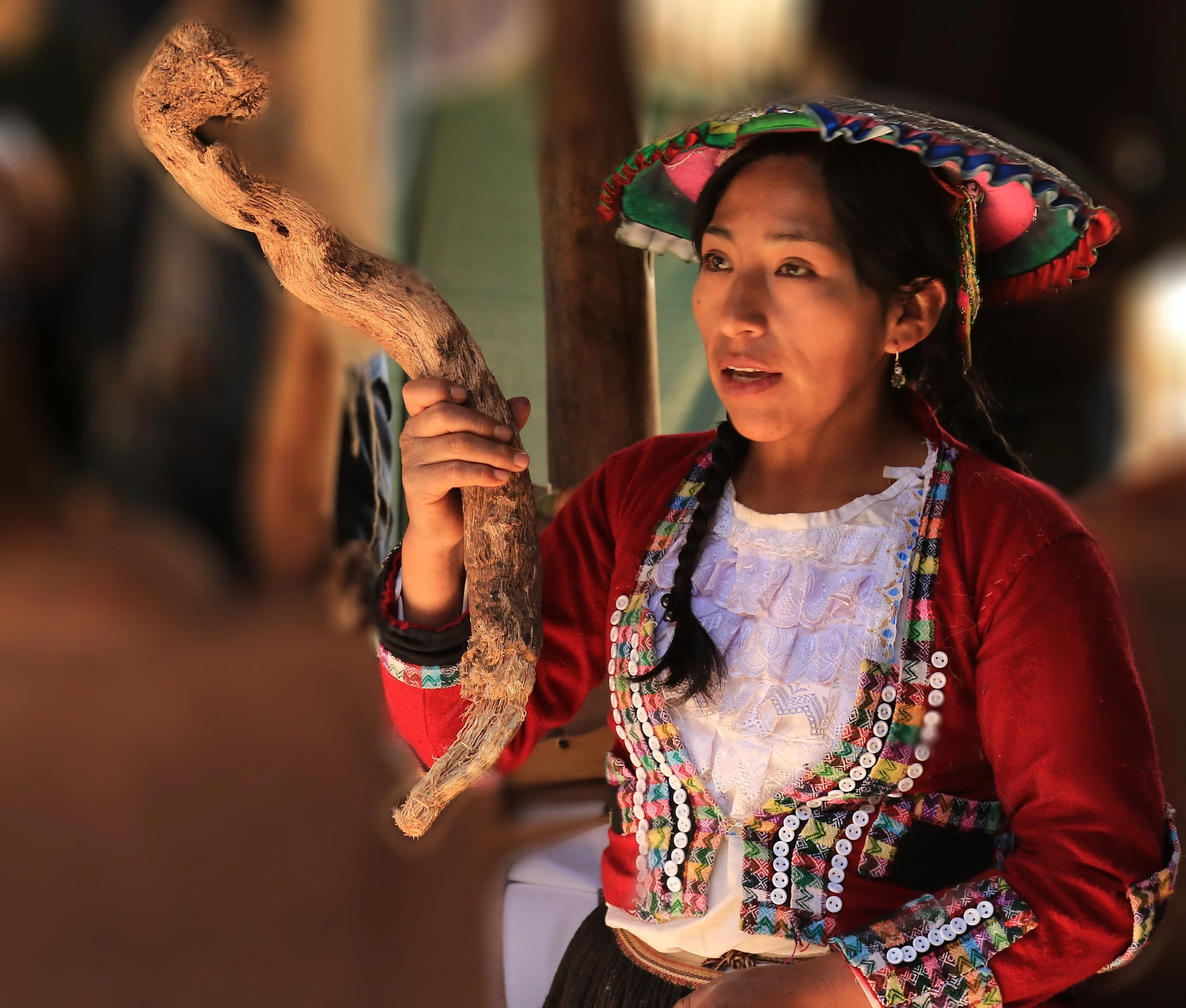 A woman wearing traditional clothing and a colorful hat, holding a wooden staff and engaging in conversation.