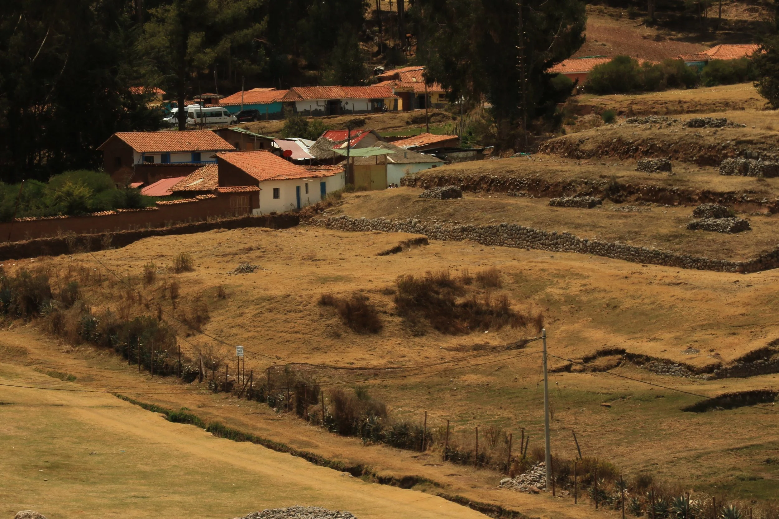Hilly landscape with scattered small houses and terraced land, some with tiled roofs, and power lines in a rural area.