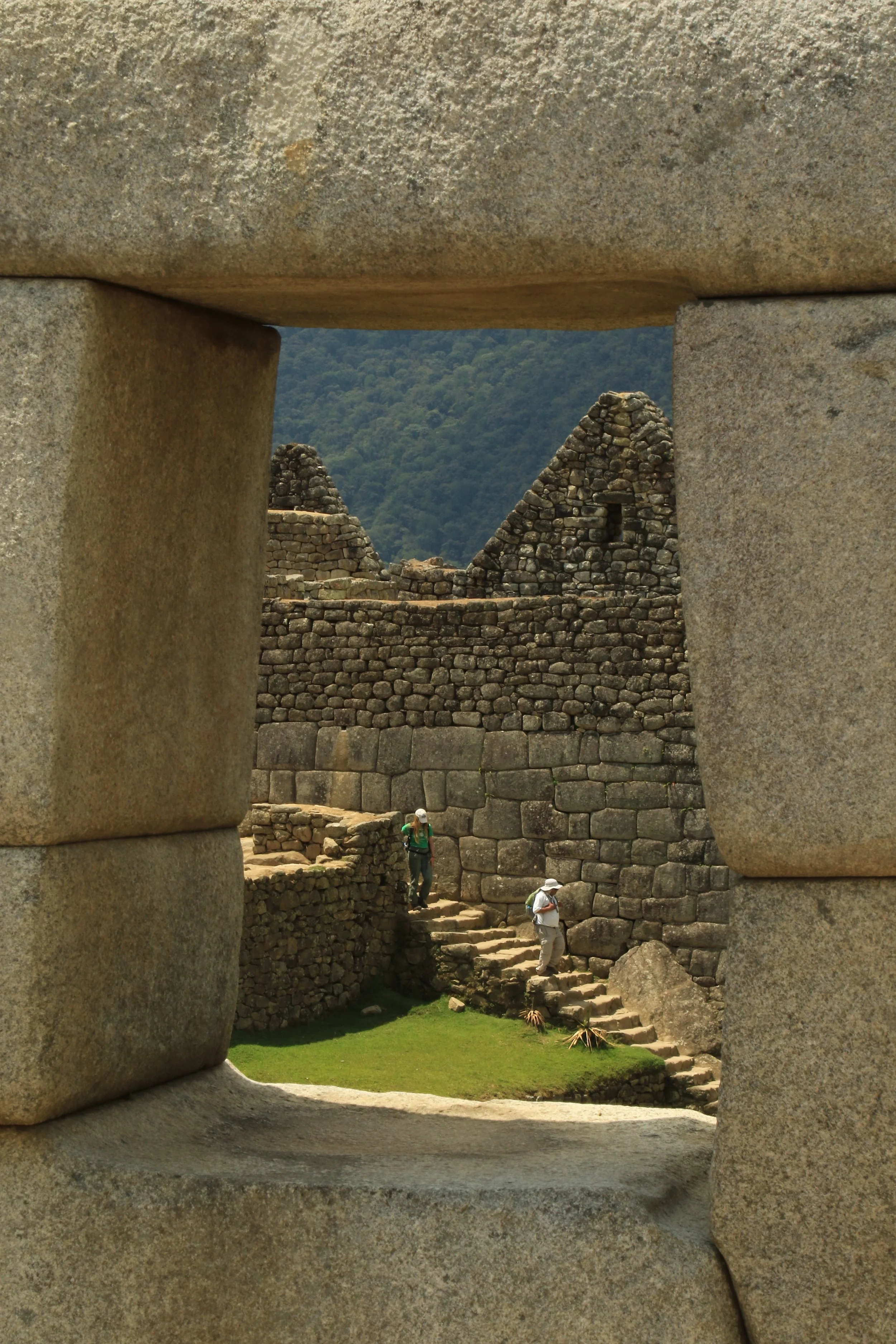 Ancient Incan ruins at Machu Picchu viewed through a stone window with two tourists exploring the site.