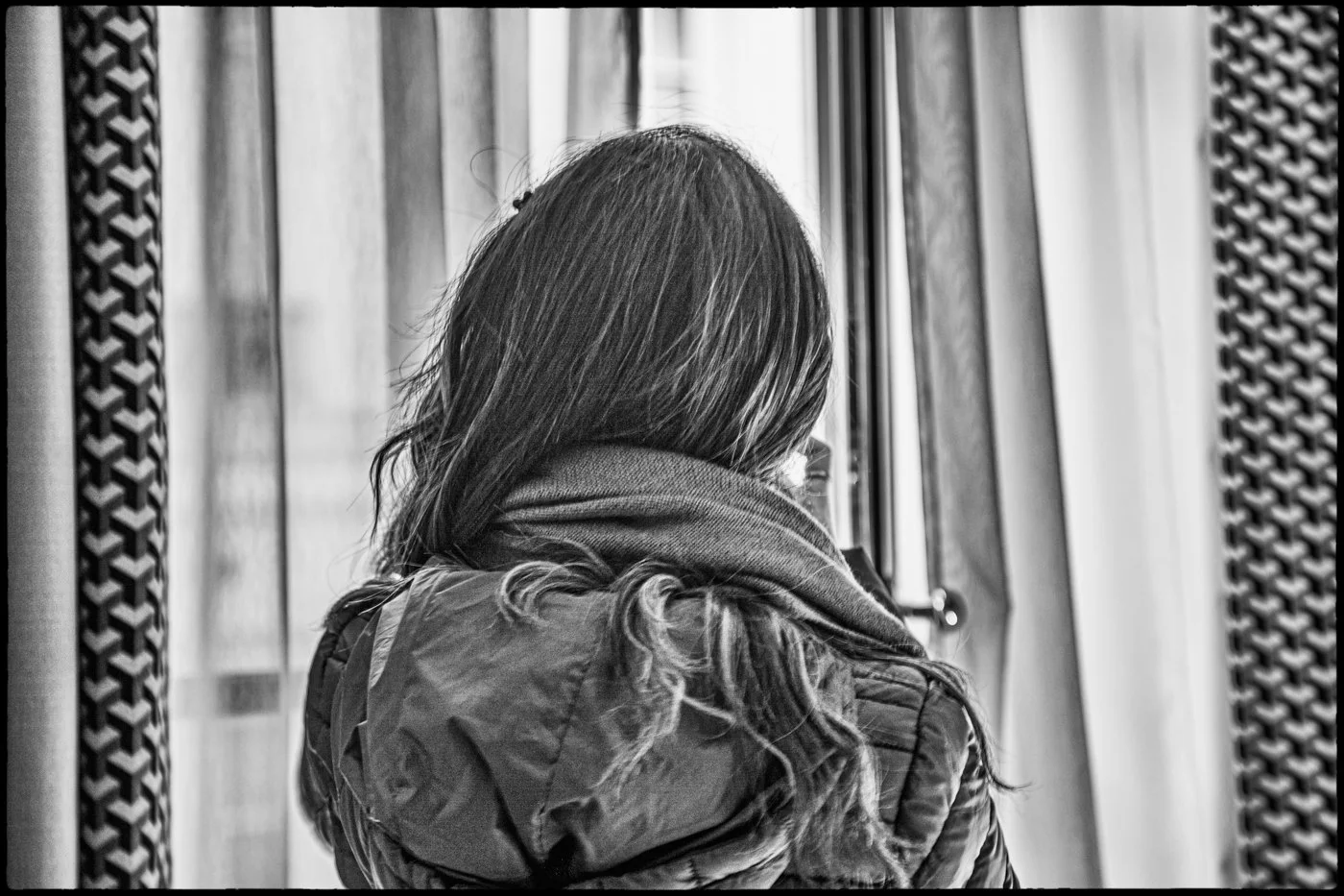 A woman with long hair wearing a jacket and scarf, sitting on a bus or train, looking out the window.