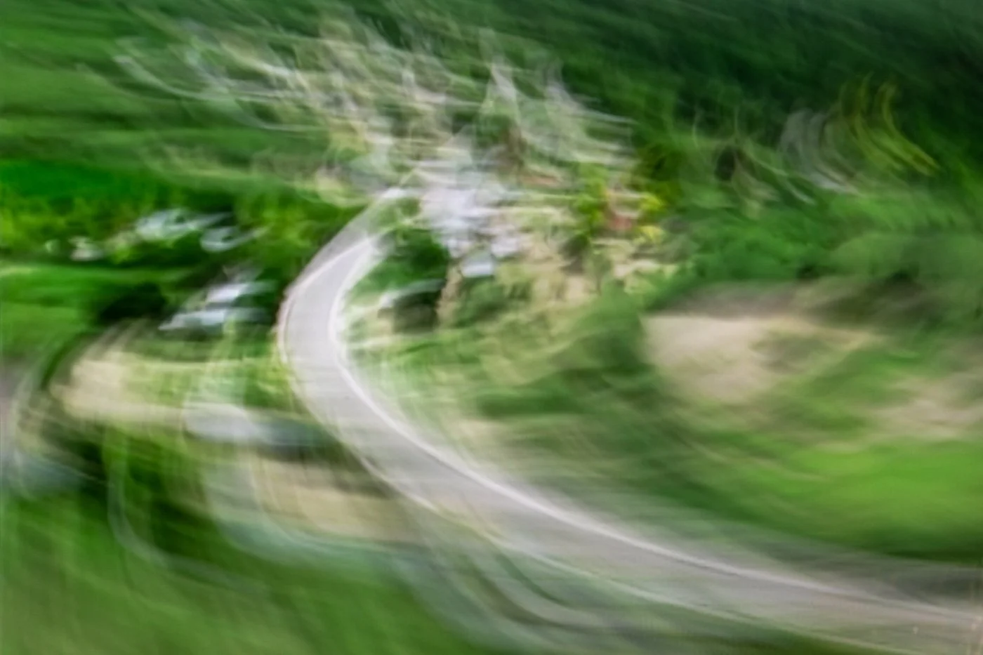 Blurred aerial view of a winding road surrounded by green trees and vegetation.