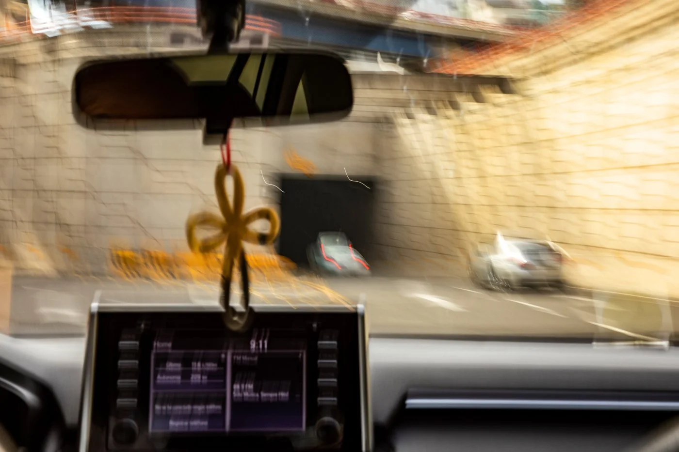 View from inside a vehicle looking through the windshield at a parking garage entrance with cars and brick walls.