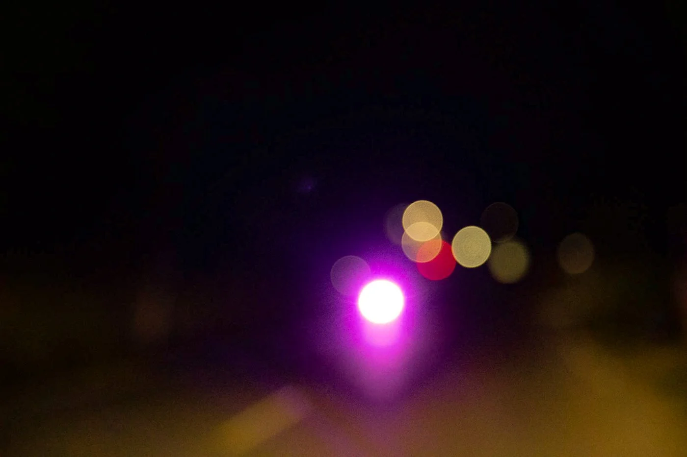 Blurred city lights at night with a bright purple and white light reflection on water.