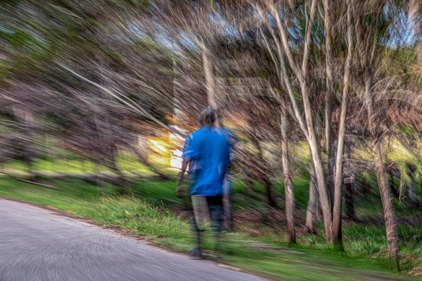 A person walking on a sidewalk near trees with blurred motion effect.