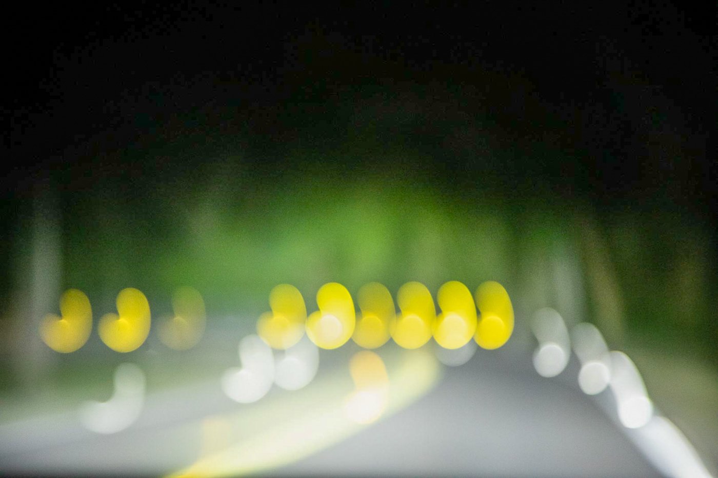 Blurred nighttime view of a road with yellow and white streetlights creating bokeh effects.