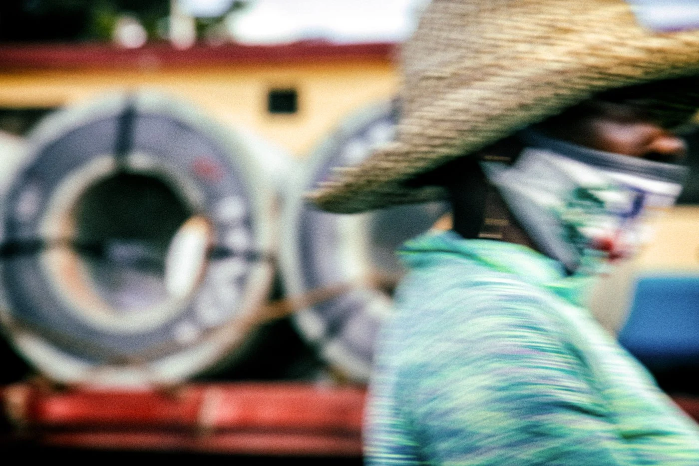 A man wearing a mask and a hat with broad brims is visible in front of a large machine with a circular component.