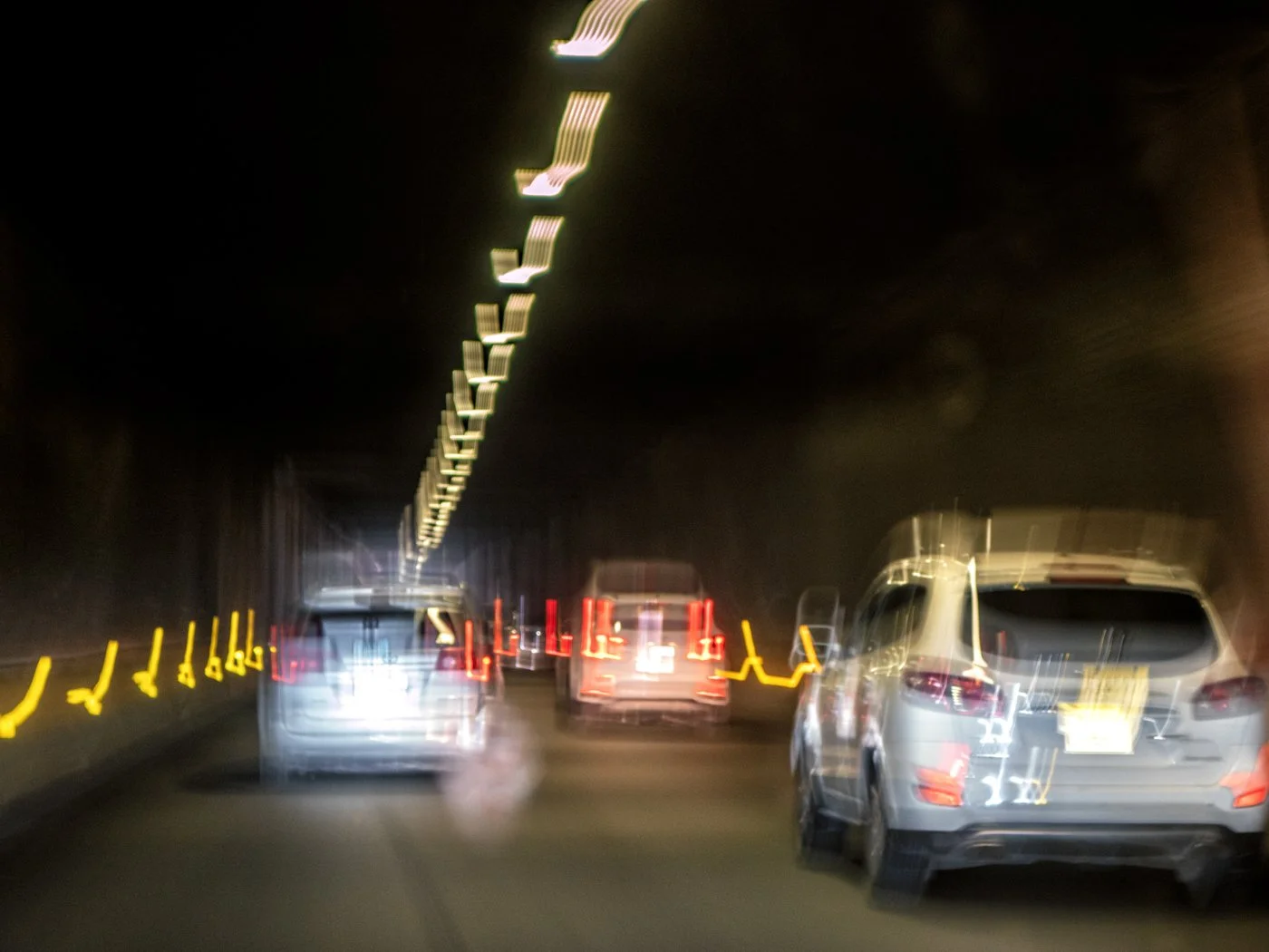 Blurry photo of vehicles moving through a tunnel at night, with streaks of illuminated road markings and ceiling lights.