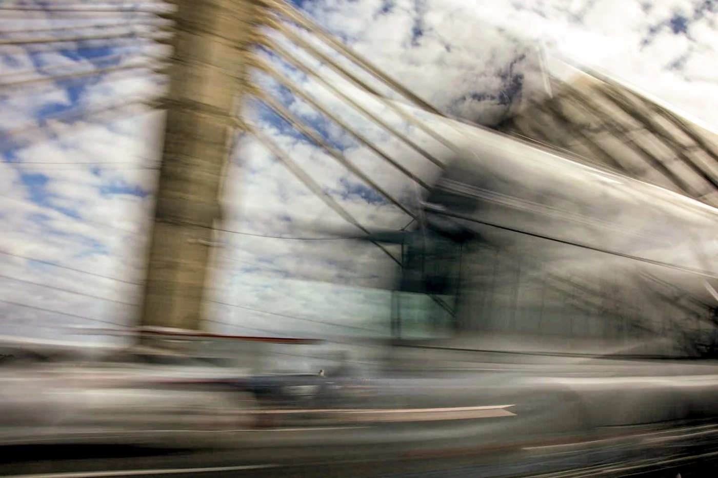 Blurred view of a modern glass bridge with clouds and sky reflecting on its surface, giving a sense of motion.