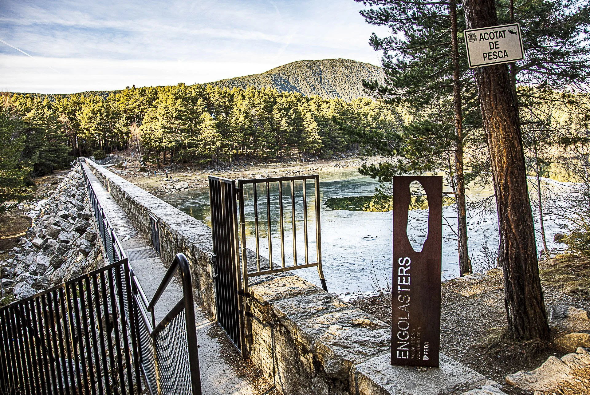River with a dam and a walkway, surrounded by trees and a mountain in the background.