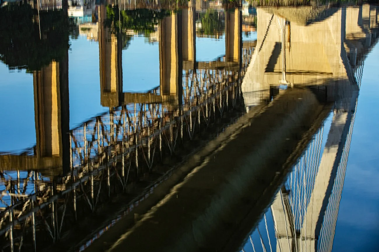 Reflection of a cable-stayed bridge in water, showing the bridge's cables and towers.