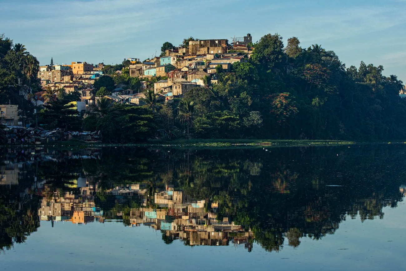 Hilly residential area with colorful houses and lush greenery reflected in a calm body of water.