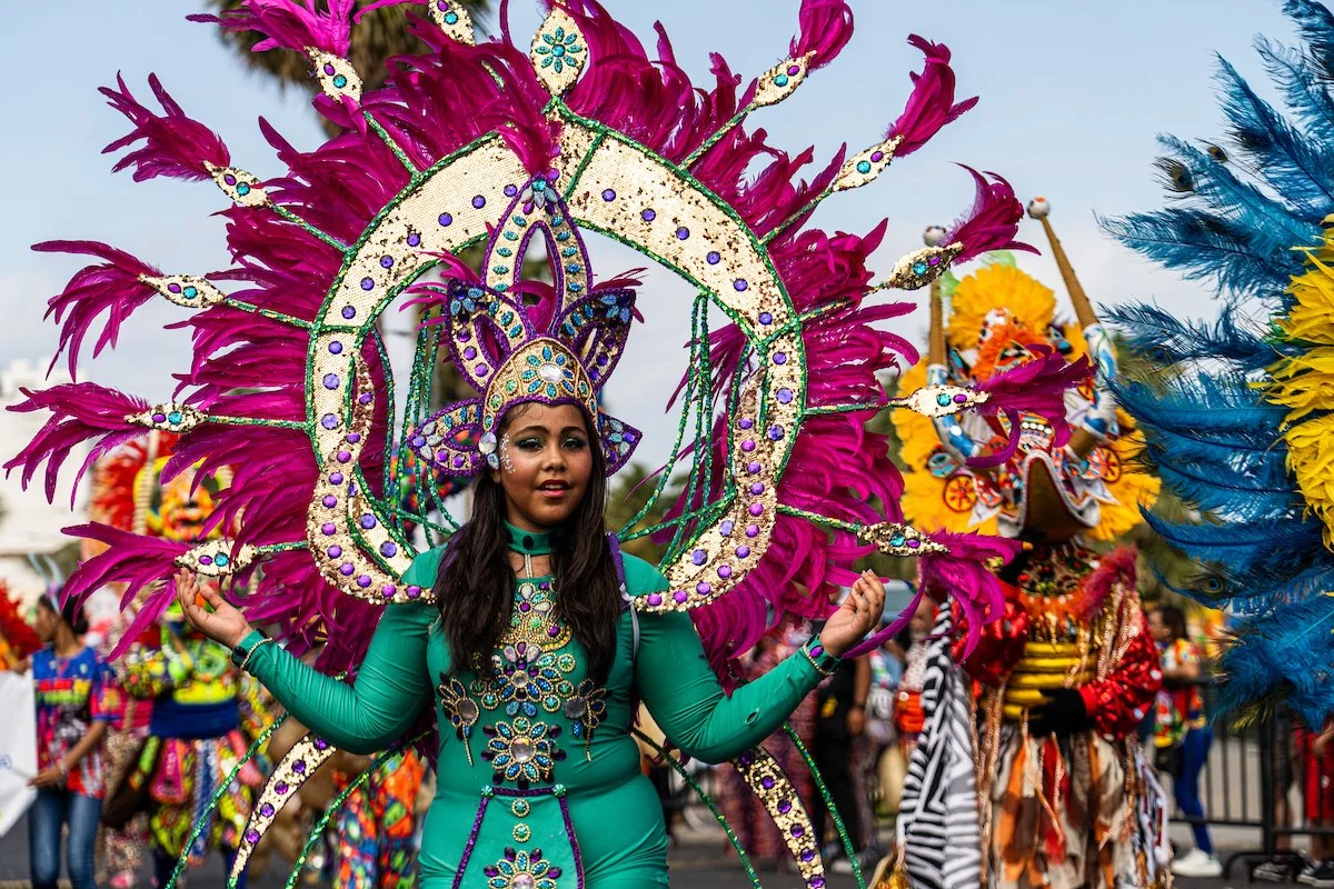 Woman in a vibrant green costume with an elaborate pink feathered headdress at a cultural parade or festival.