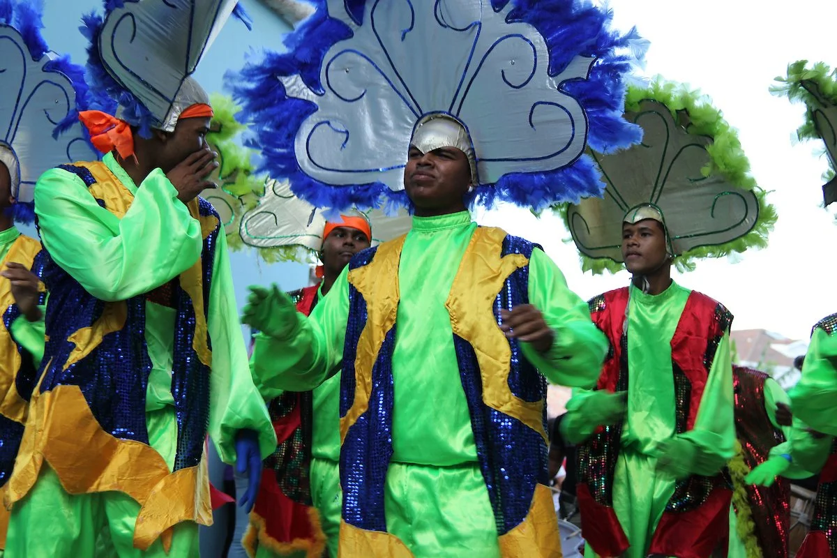People in colorful costumes with feathered headdresses participating in a parade or festival.