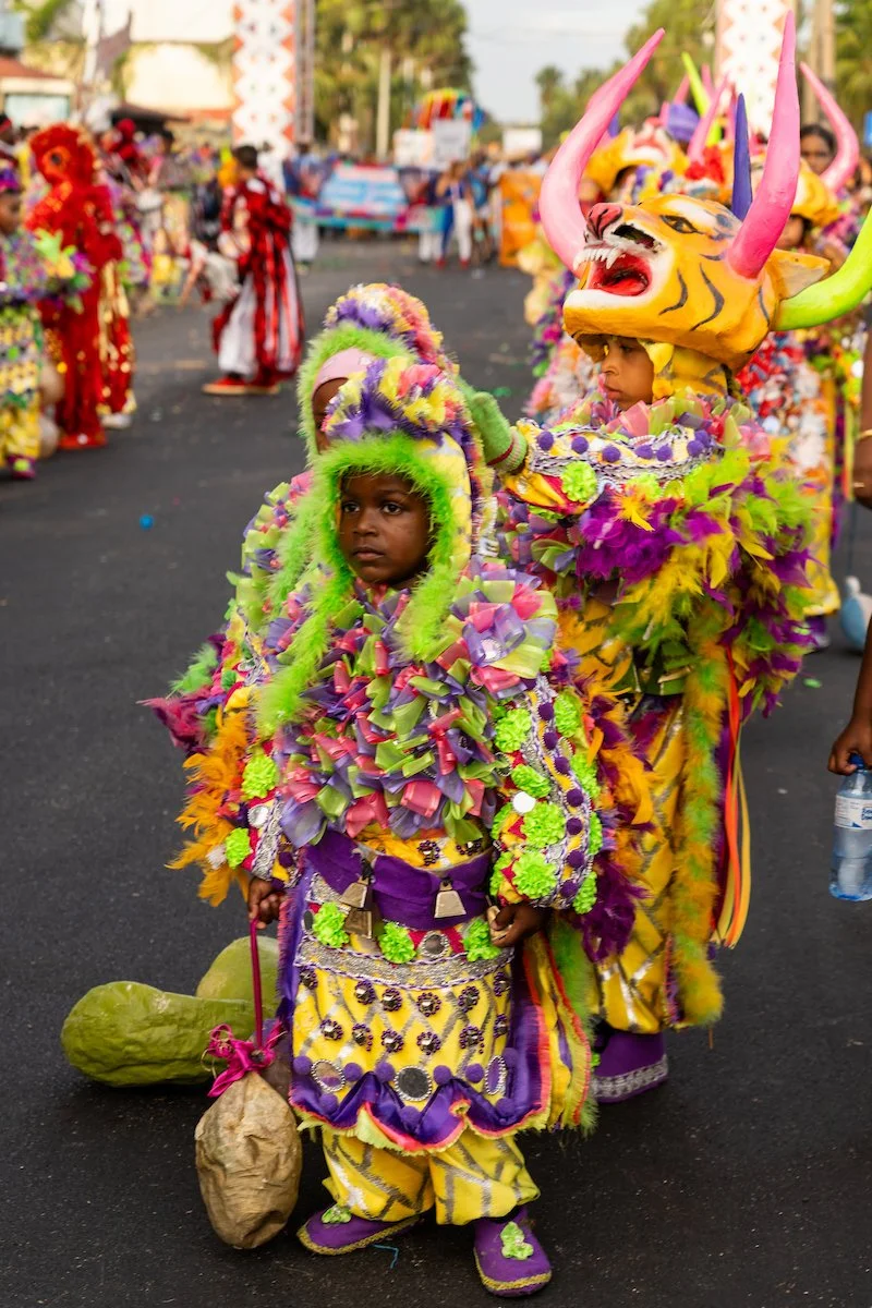 Children dressed in colorful elaborate costumes with masks and headdresses participating in a parade or festival.