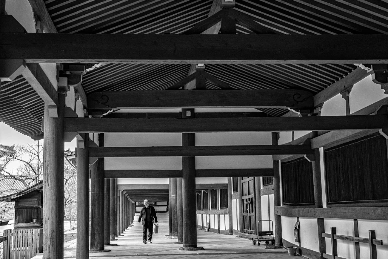 A person walking through a traditional Japanese wooden corridor with pillars and a tiled roof.