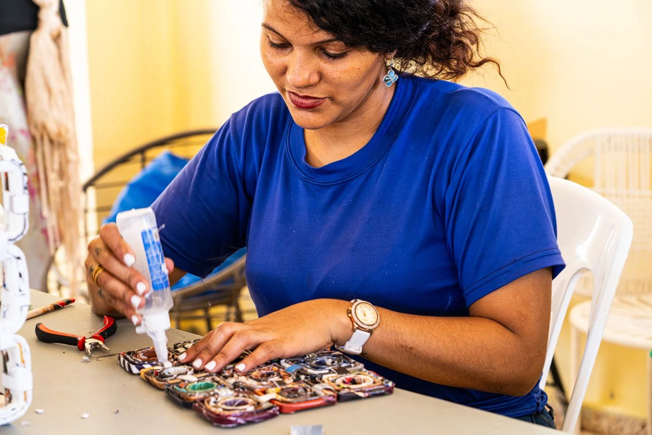 Woman in a blue shirt assembling or repairing decorated phone cases at a work desk.