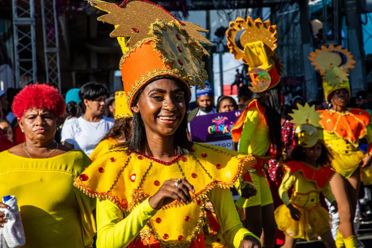 People participating in a parade, dressed in colorful yellow costumes with ornate hats, during a cultural celebration.