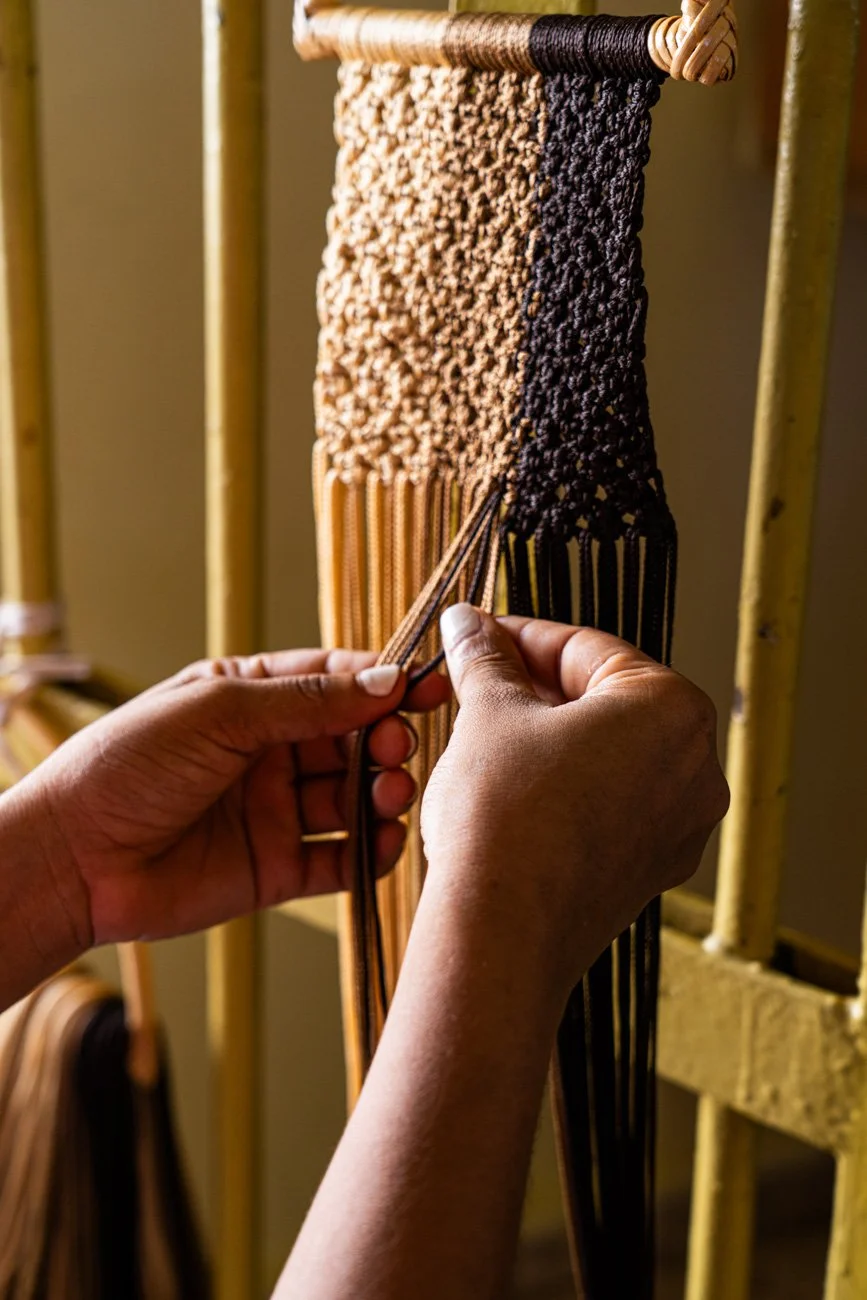 Person weaving a piece of fabric or textile on a loom.