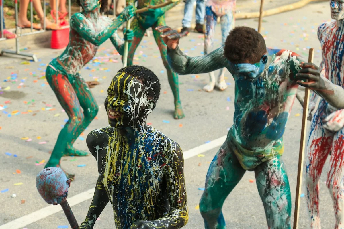 People celebrating Holi with colorful powder and paint, covered in splashes of vibrant colors, in an outdoor setting with confetti on the ground.