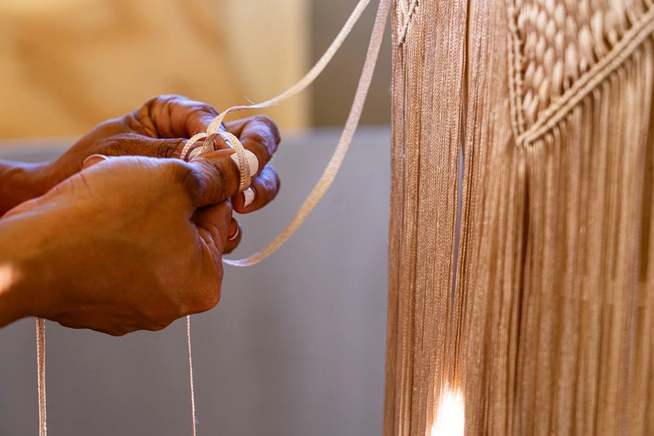 A person sewing or working on a piece of fabric with beige or peach-colored threads in close-up view.