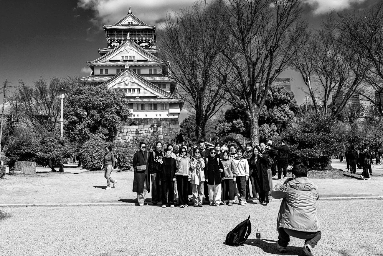 A group of people taking a photo in front of Osaka Castle. The scene is in black and white.