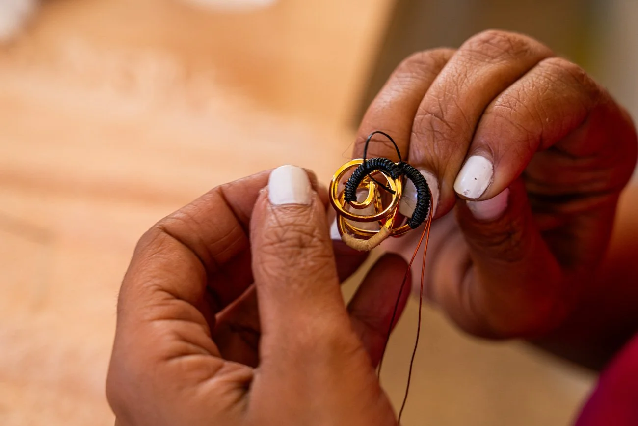 Close-up of a person’s hands holding a small, intricate craft made of coiled wire and wrapped thread, with some parts being black, yellow, and beige.