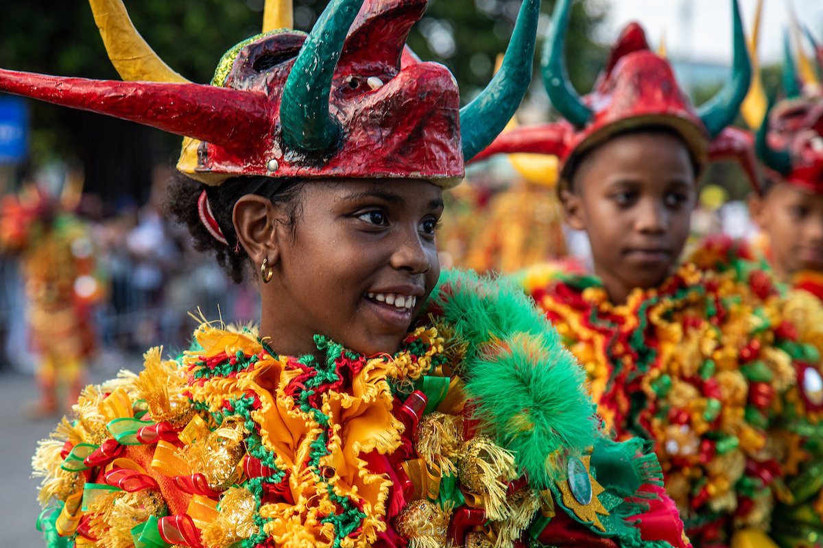 Children dressed in colorful costumes with large, decorated hats participating in a festive parade or celebration.