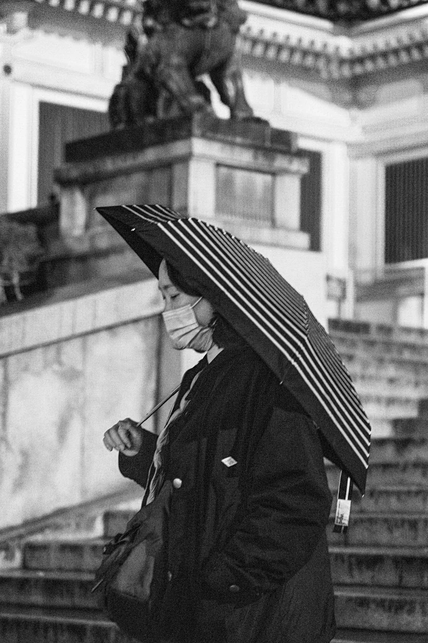 A woman wearing a face mask and carrying an umbrella walking down stairs in an urban setting at night.