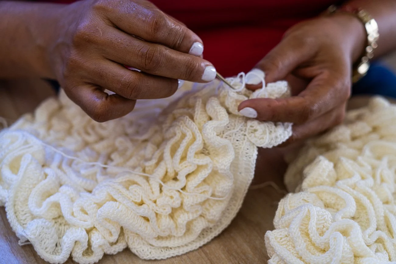 A person knitting with cream-colored yarn, using a knitting needle.