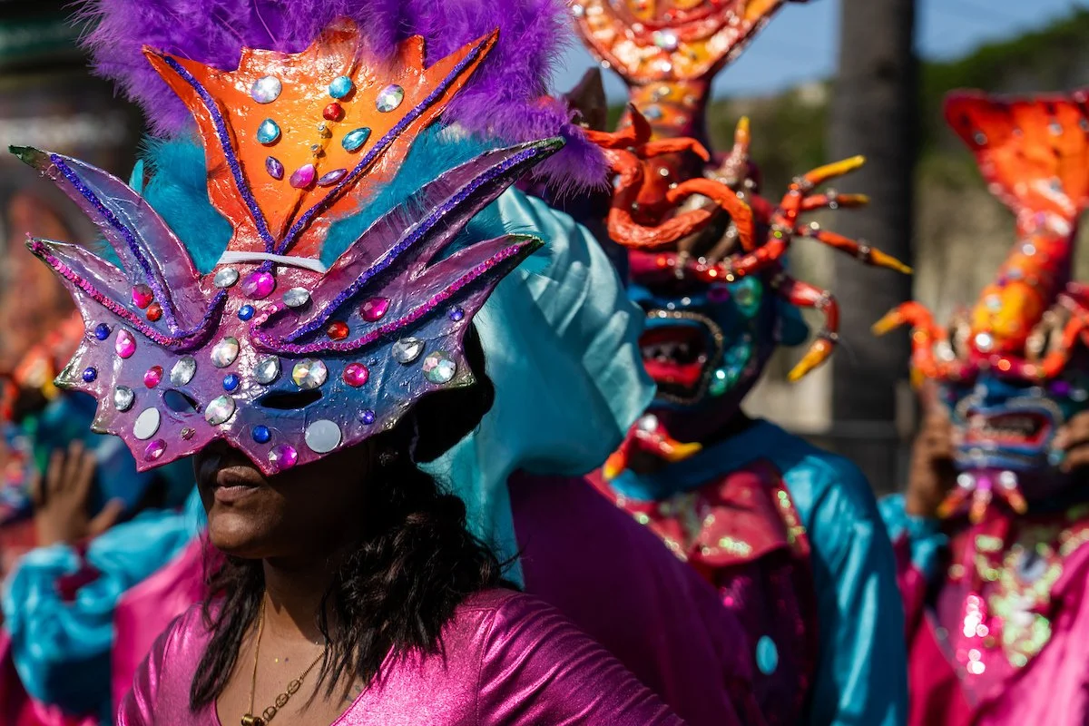 People participating in a carnival or festival, wearing colorful costumes and elaborate masks adorned with rhinestones and feathers.
