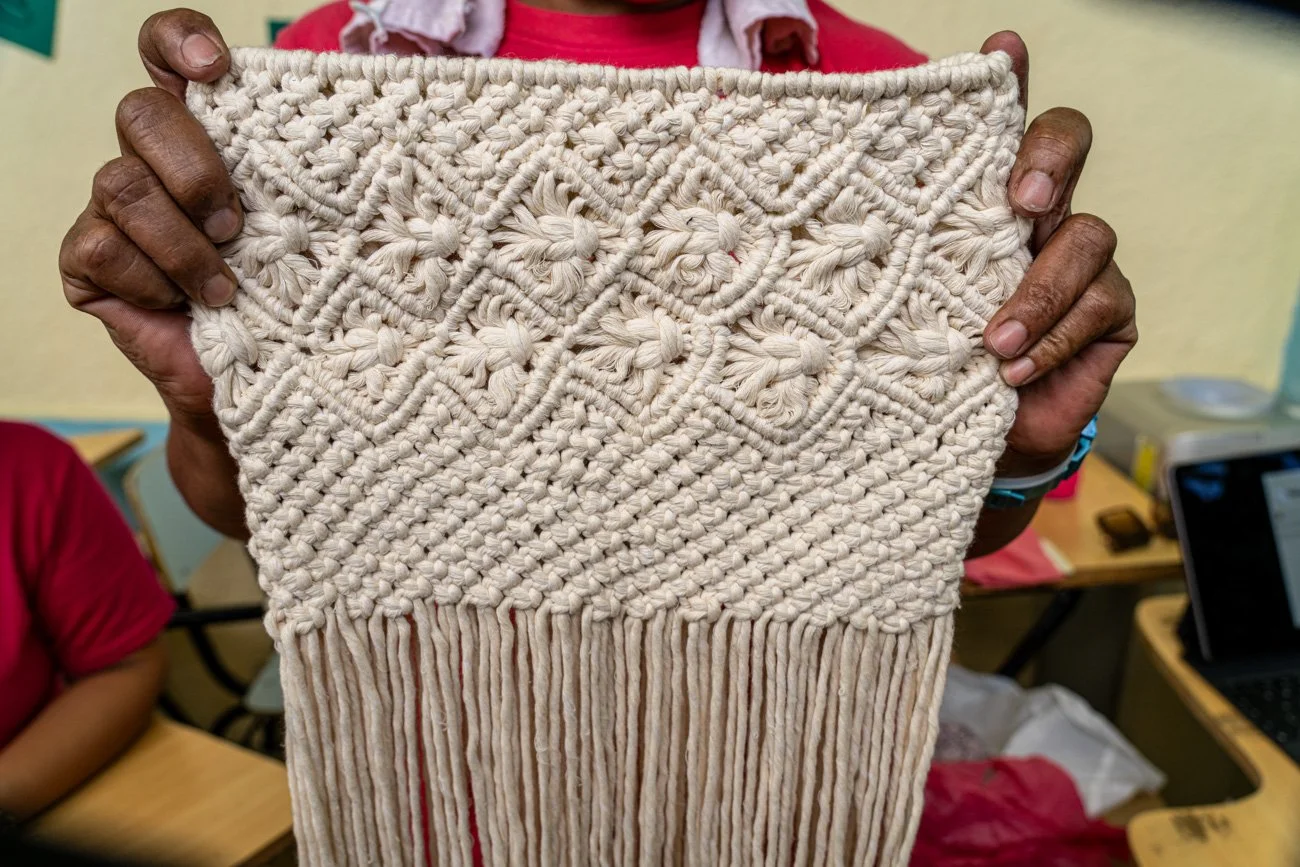 Person holding an intricate handmade macramé wall hanging with geometric patterns and fringe.