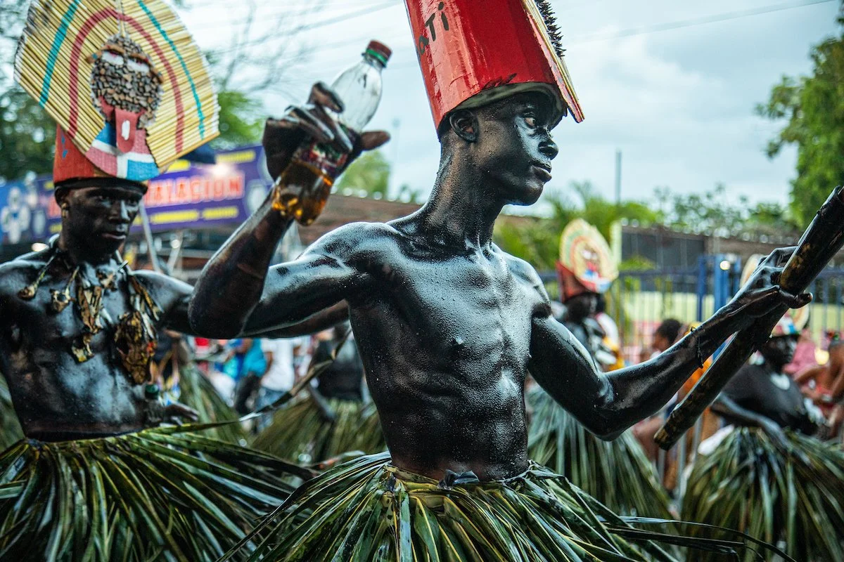 Men dressed in traditional tribal attire, with body paint and grass skirts, participating in a cultural parade or festival.
