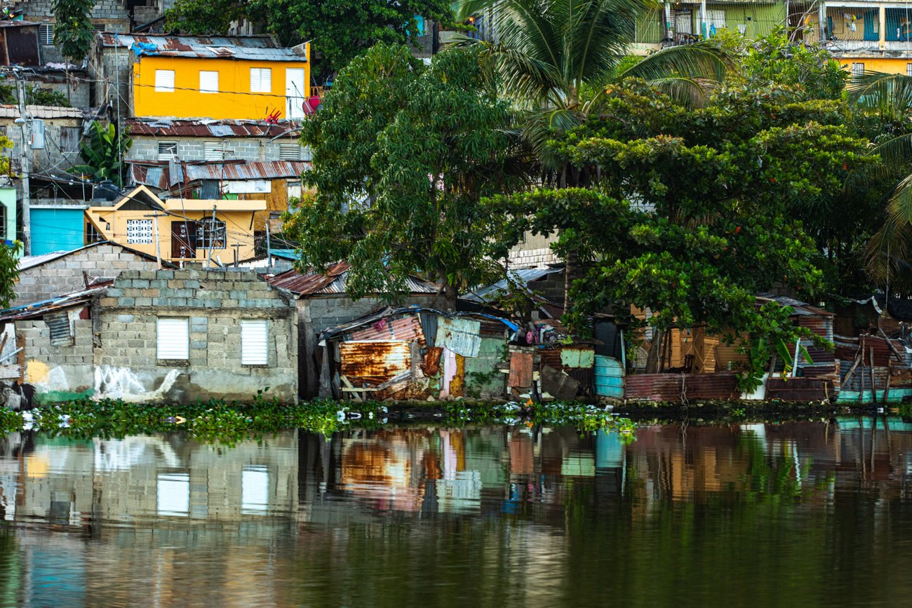 A riverside community with colorful houses, trees, and a reflection on the water.
