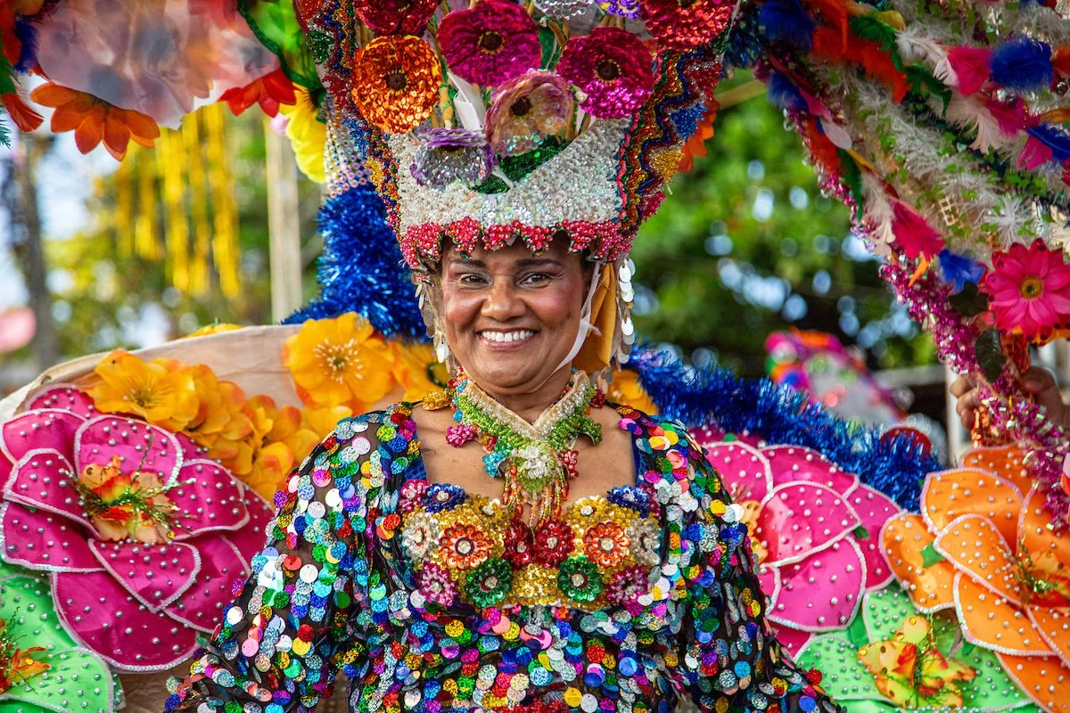 Woman dressed in colorful, beaded, and feathered costume smiling during a festival or parade.