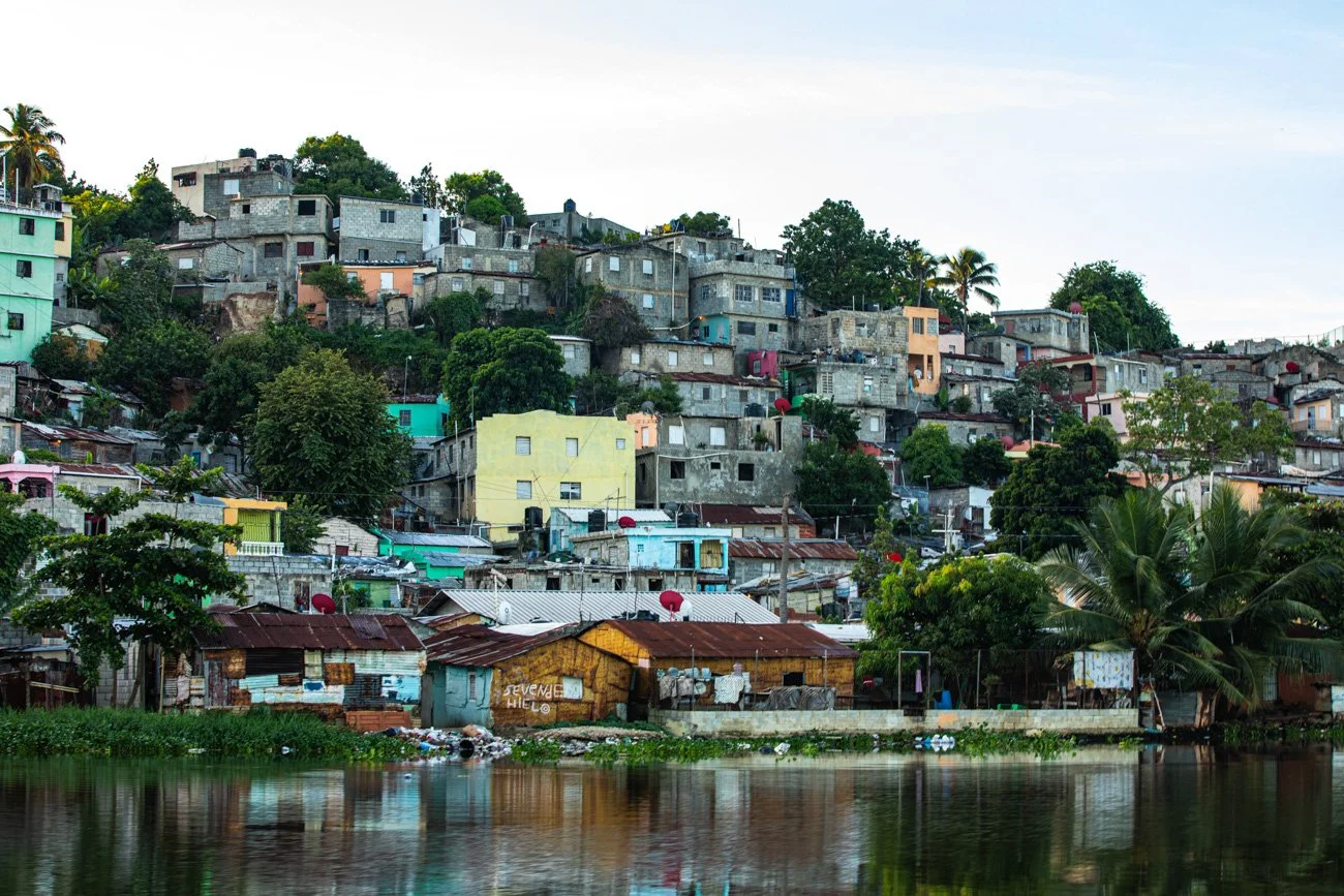 Hilly hillside neighborhood with colorful houses and lush green trees, located by a body of water, under a partly cloudy sky.