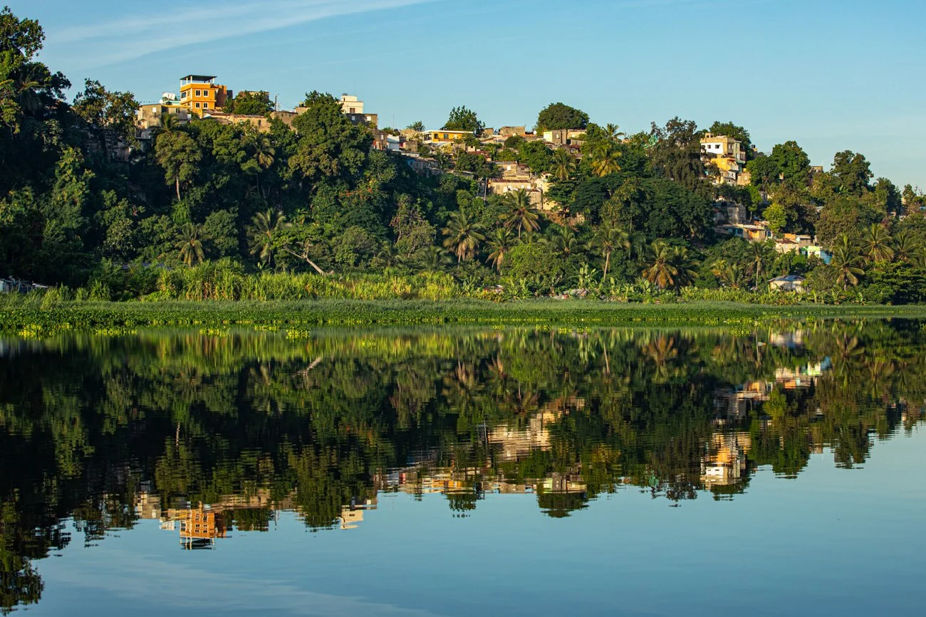 Hillside neighborhood with houses and lush greenery reflected in a calm body of water.