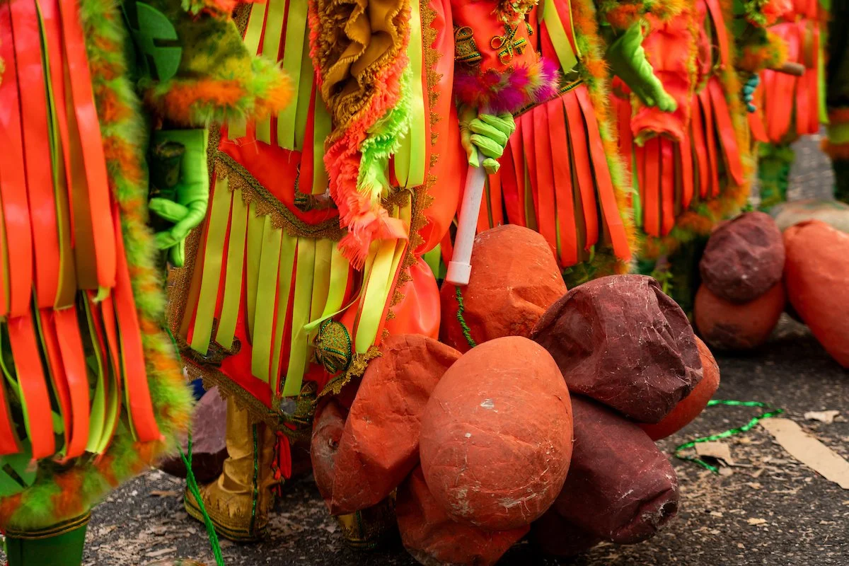 Colorful parade costumes with yellow and red ribbons, furry fabric, and gold accents, placed on a ground with large reddish rocks.