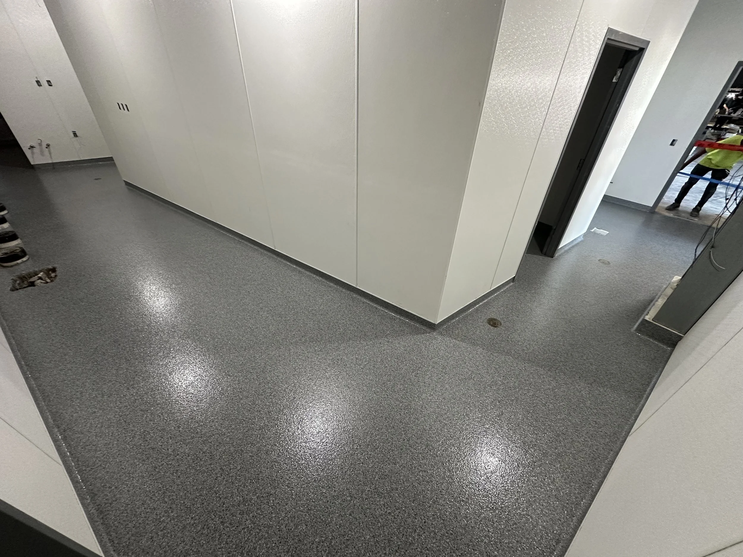 Commercial or industrial space with a solid dark gray epoxy floor and wall mounted electrical sockets