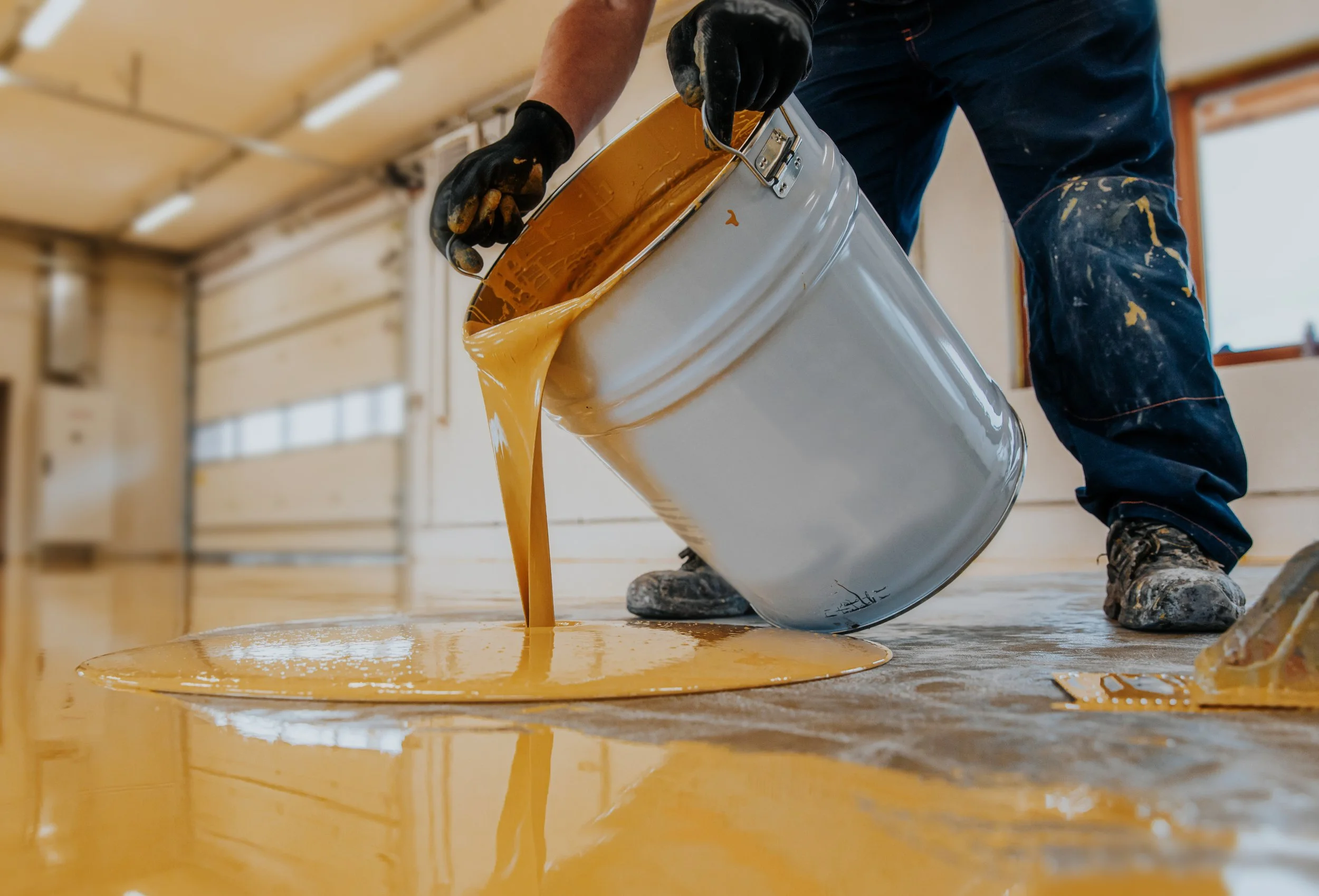 Technician pouring amber-toned epoxy coating during floor installation in Kansas City