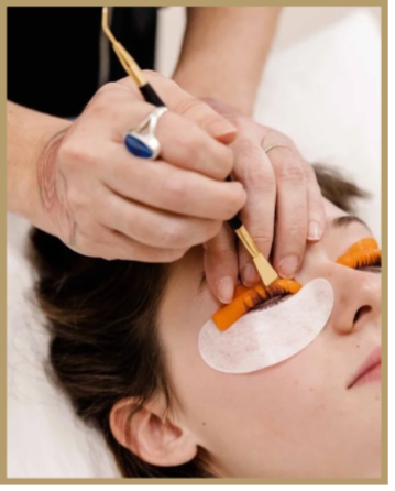 A person receiving eyelash extension or eyelash tinting treatment with technician applying product near the eye while the client has eye pads under her eyes.
