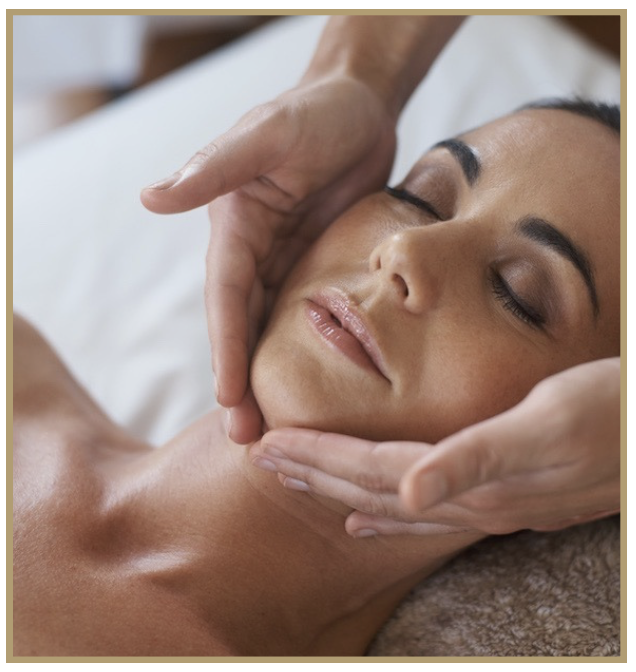 A woman receiving a facial massage from a massage therapist, lying with eyes closed on a massage table.