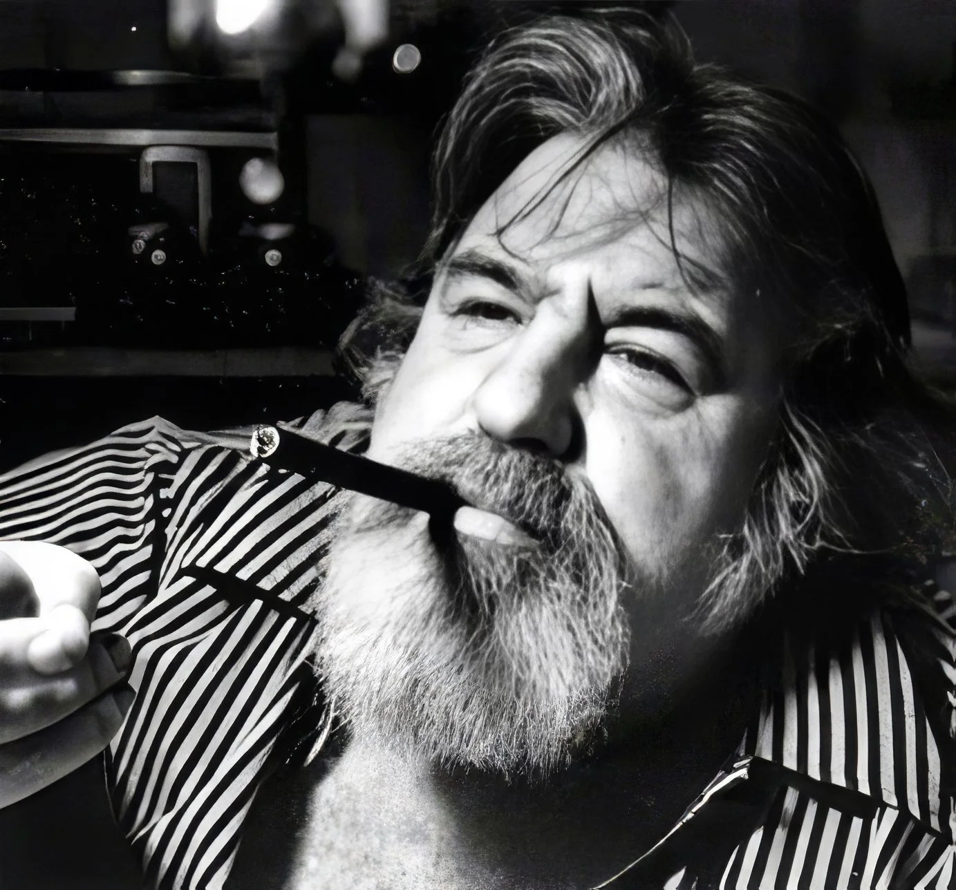 Black and white close-up photograph of Doc Pomus with long hair and a beard, holding a cigar near his mouth, wearing a striped shirt.